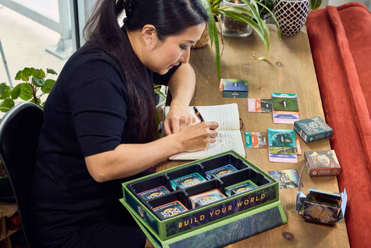 A woman is writing and using the Story Engine: Deck of Worlds